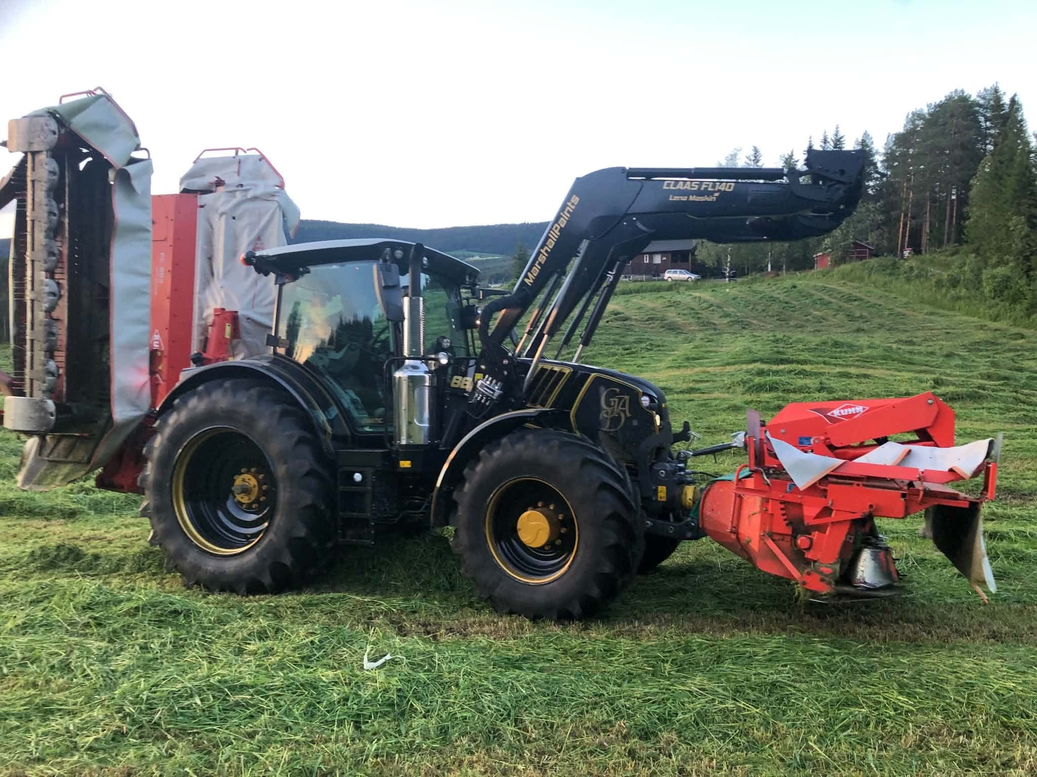 Svart traktor med frontlastar og raud slåmaskin på tunet